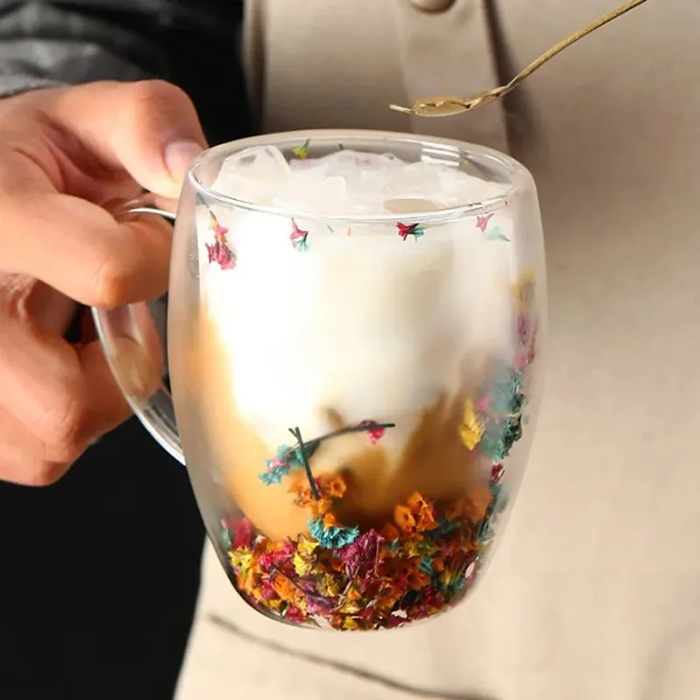 Foto-Caneca-Flor-Seca-CB-89372-Imagem-3.png Mão segurando xícara com flores secas e bebida cremosa