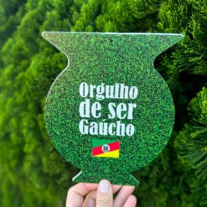 Vira-mate verde com mensagem gaúcha, segurado diante de folhagem
