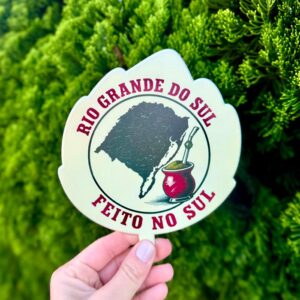 Vira-mate formato folha com ilustração de cuia, segurado diante de folhagem verde